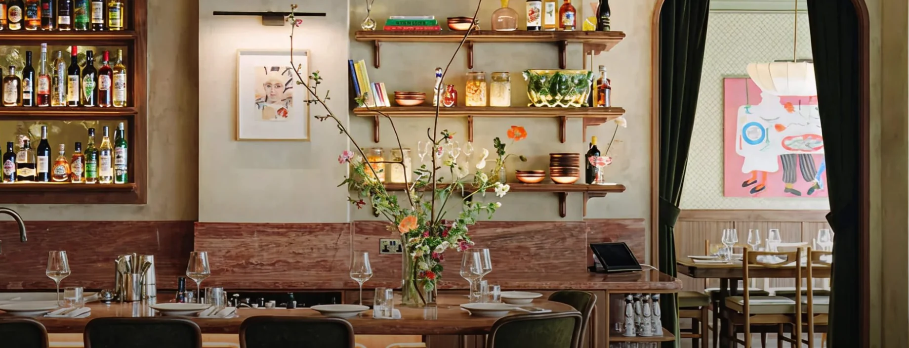 A restaurant bar with shelves of bottles, flowers and an arched doorway, designed by B3 Designers